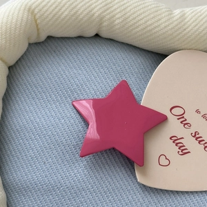 Macro detail of a glossy magenta star hair clip on soft blue fabric with a pink card