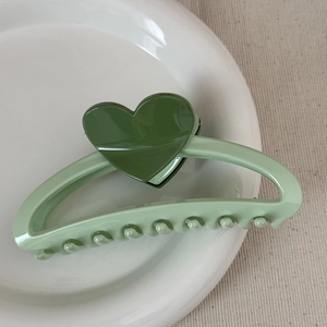 Detail of light green claw clip with dark green hearts on a white ceramic tray