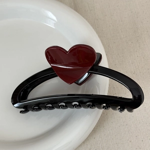 Detailed close-up of a glossy black heart hair claw clip on a white ceramic plate