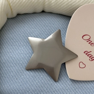 Close-up of a glossy silver Y2K star-shaped hair clip on light blue twill fabric background