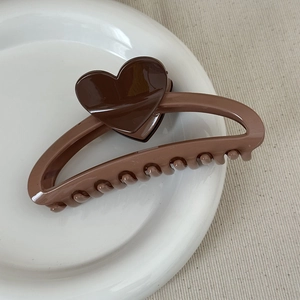 Detail shot of a brown heart-shaped hair claw clip on a white ceramic tray display