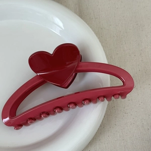 Detail shot of a glossy deep red heart hair claw clip on a white ceramic plate