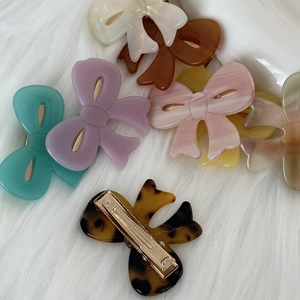 Bow-shaped acetate hair clips in assorted marble textures and colors on faux fur background