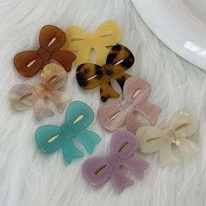 Flat acetate bow hair clips in eight assorted marble patterns on soft white plush background