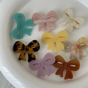 Set of 8 colorful acetate bow hair clips in pastel tones on a white ceramic plate