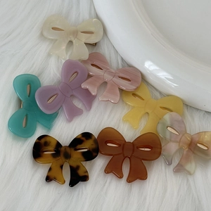 Flat bow hair clips in acetate multiple colors on a soft white faux fur background
