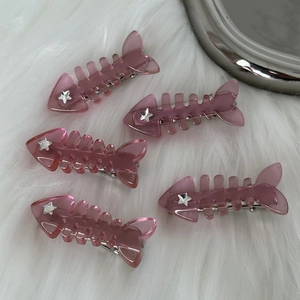 Detail showing five pink translucent fishbone hair clips with silver star accents on fur