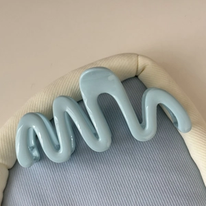 Vue détaillée d'une pince à cheveux ondulée bleu clair sur tissu en velours côtelé