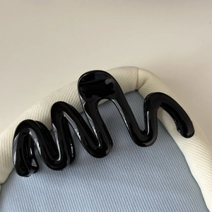 Gros plan d'une pince à cheveux noire brillante en forme de vague sur tissu bleu
