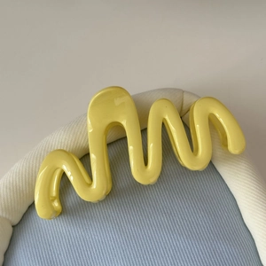 Détail d'une pince à cheveux ondulée jaune citron sur un plateau rayé bleu clair