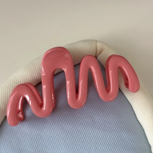 Détail d'une pince à cheveux rose ondulée avec finition brillante sur fond texturé