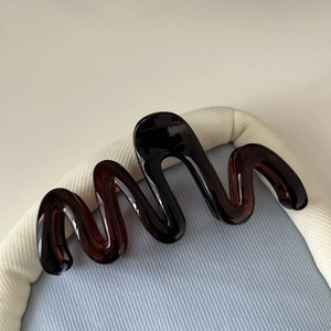 Gros plan détaillé sur la pince à cheveux ondulée en résine ambrée au design moderne brillant