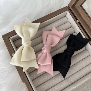 Detailed close-up of bow hair clips in cream, pink and black within a velvet jewelry box