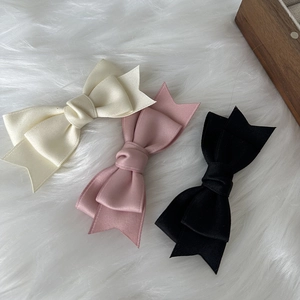 Detailed close-up of ribbon bow hair clips in cream, pink and black textured fabric