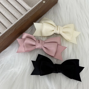 Three elegant bow hair clips in cream, pink and black on soft faux fur background