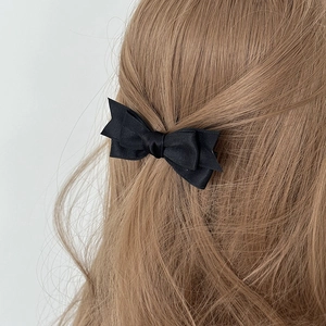 Detailed view of a double-layered black satin bow hair clip on wavy brown hair
