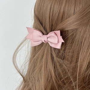 Elegant light pink double-layered satin bow hair clip worn on long wavy brown hair