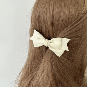 Sweet cream white ribbon bow hair clip worn on long wavy brown hair for styling