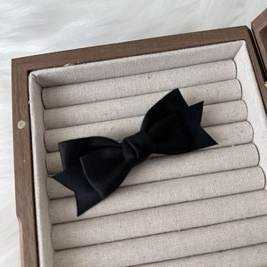 Detail of a black satin double-layered bow hair clip placed in a wooden jewelry box