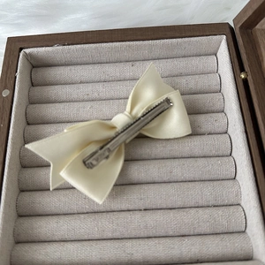 Detail view of cream satin bow hair clip showing smooth texture and metal duckbill clip