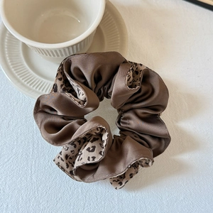 Gros plan sur les textures léopard et satin marron d'un chouchou à cheveux plissé