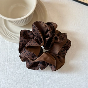 Détail d'un chouchou en satin à motif léopard marron sur fond texturé blanc