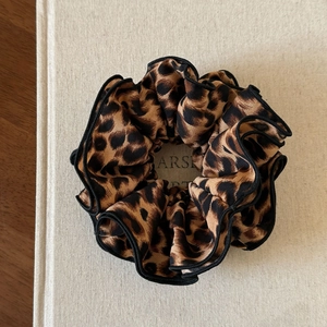 Detail view of leopard print scrunchie with black ruffled edges on a textured book
