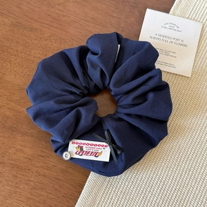 Detail of dark blue scrunchie with vintage label, black ribbon bow, and silver button