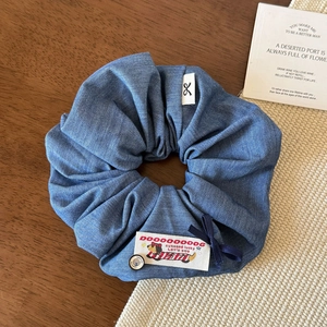 Close-up of blue denim scrunchie with cute embroidery and a metal button on wood