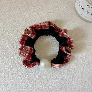Detail of checkered plaid scrunchie with a large faux pearl on soft white fabric