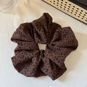 Close-up of a large leopard print scrunchie on a white textured fabric background
