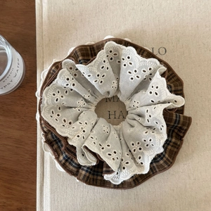 Détail d'un chouchou à carreaux marron avec dentelle blanche sur fond beige neutre