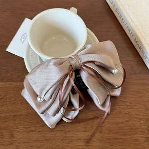 Détail d'une pince à cheveux nœud champagne avec perles et rubans sur table bois