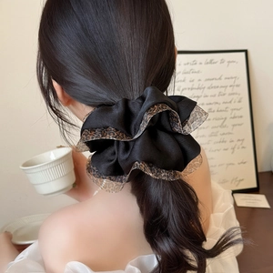 Black satin scrunchie with leopard print lace trim shown on a ponytail in a cozy setting