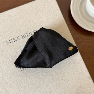 Détail d'une pince à cheveux en tissu noir avec texture à pois et logo doré élégant