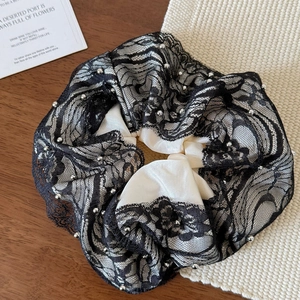 Close-up of black floral lace scrunchie with silver bead detailing and white satin