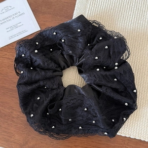 Close-up of black satin scrunchie with lace edges and silver beads on a wooden desk