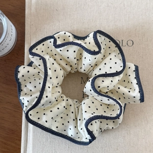 Detailed texture of large beige satin scrunchie with navy blue polka dots and ruffle edges