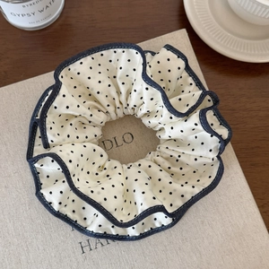 Detailed close-up of a satin polka dot hair scrunchie with navy blue piping on a book