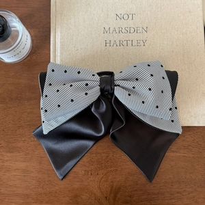 Elegant layered bow hair clip with black stripes and polka dots on a wooden desk