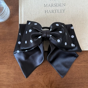 Polka dot satin bow hair clip with long ribbons on a vintage wooden desk setup
