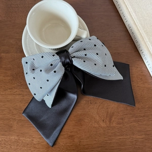 Close-up of elegant bow hair clip with black and white stripes and polka dots on wood