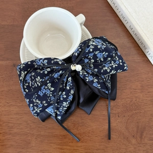 Detail view of a floral bow hair clip with a heart pendant on a wooden table surface