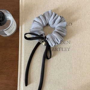 Detail van grijze geplooide scrunchie met zwarte strik, parel en kleine kristallen