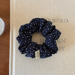 Detail of navy blue pleated scrunchie with white patterns and gold heart charm