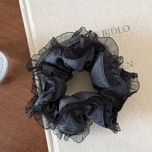 Détail d'un chouchou en dentelle noire avec texture denim sur un livre en tissu beige