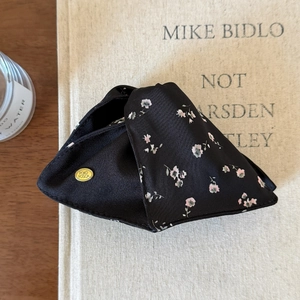 Detail showing elegant black floral fabric accessory with gold engraved logo plaque