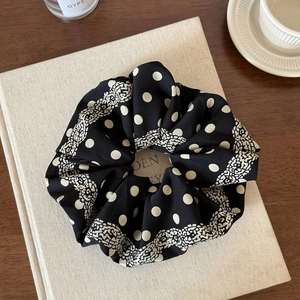 Polka dot black fabric scrunchie with lace edge and elastic hair tie on a book