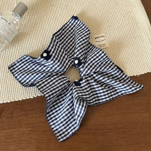 Close-up of blue and white checkered scrunchie with floral detail on a rustic background