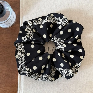 Detailed macro view of black paisley and polka dot satin scrunchie on beige book